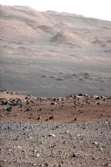 The gravelly area around Curiosity's landing site is visible in the foreground. Farther away, about a third of the way up from the bottom of the image, the terrain falls off into a depression (a swale). Beyond the swale, in the middle of the image, is the boulder-strewn, red-brown rim of a moderately-sized impact crater. Farther off in the distance, there are dark dunes and then the layered rock at the base of Mount Sharp. Some haze obscures the view, but the top ridge, depicted in this image, is 16.2 kilometres away.