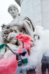 Pro-Palestinian protesters brandish flares with the colors of the Palestinian flag as they stand on a monument at Place de la Republique in Paris, France, during a banned demonstration in support of Gaza.
