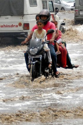 A motor-cyclist and his passengers travel along a water-logged road as the first monsoon rains arrive in Jalandhar on June 7, 2012.  The monsoon rains brought relief from the scorching heat wave.