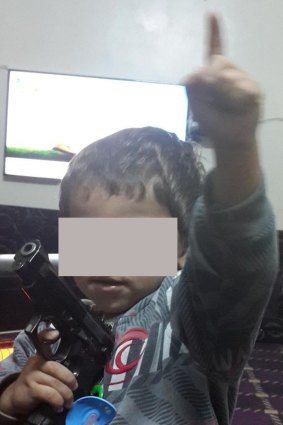 The picture of the young boy with a gun and dummy and doing the Islamic State salute. 