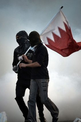 Bahraini protestors carry the national flag as they run for cover from tear gas fired by riot police in Bahrain.
