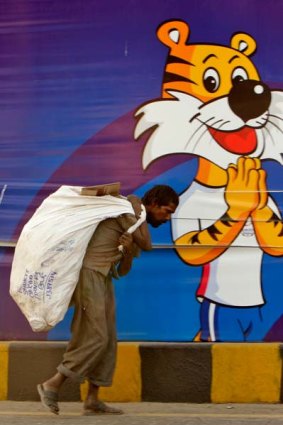 Contrasts ... a scavenger hauls a sack of recyclable rubbish past a Games mascot in Delhi.