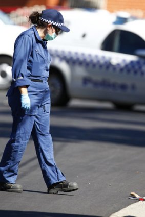 A forensics officer approaches what appears to be a tomahawk on the street.