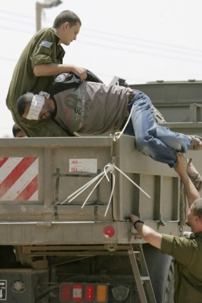 Israeli soldiers carry a blindfolded Palestinian, detained in a military operation in the Gaza Strip, onto a truck.