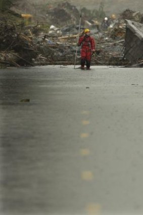 A search and rescue worker wades through water covering Washington Highway 530.