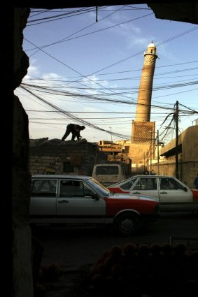 An electrician works on the roof of a shop in Mosul in 2003, in the background is the leaning minaret of the al-Nuri mosque.