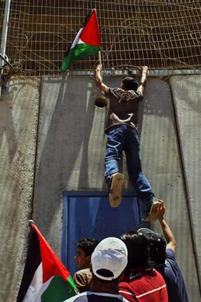A man is hoisted  by fellow protesters to hang a Palestinian flag on Israel's separation barrier in the occupied West Bank village of Beit Hanina.