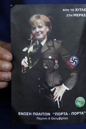 A man displays a postcard-sized poster depicting German Chancellor Angela Merkel in a Nazi uniform.