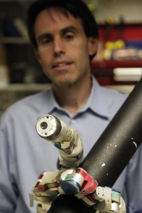 Carnegie Mellon University professor Howie Choset stands behind a robot demonstrating how it climbs up a tubular armature at their lab on campus in Pittsburgh.