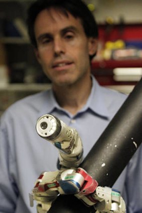 Carnegie Mellon University professor Howie Choset stands behind a robot demonstrating how it climbs up a tubular armature at their lab on campus in Pittsburgh.