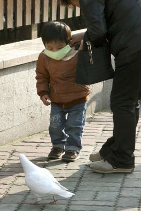 A woman helps a child adjust a face mask as they walk close to a pigeon in People Square's, Shanghai.