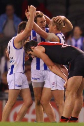 Ryan Bastinac, Drew Petrie and Liam Anthony of North Melbourne celebrate at the final siren as Jobe Watson endures the pain of defeat.