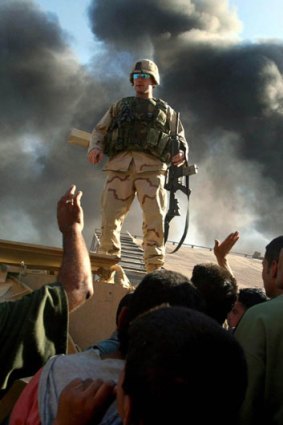 A US Army soldier warns a group of angry Iraqi civilians to disperse near where a gas station erupted into flames, in Baghdad, May 2003.