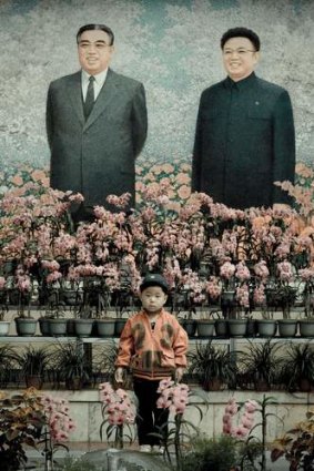 Big brothers: A boy poses in front of a fresco of Great Leader Kim Il-Sung and Dear Leader Kim Jong-il.