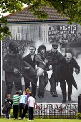 Children play in front of a mural that shows a priest carrying the body of shooting victim Jackie Duddy during Bloody Sunday in 1972.