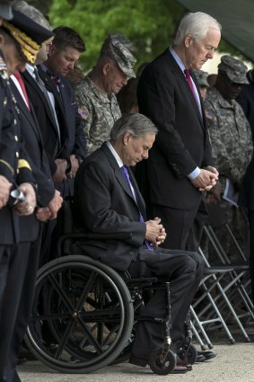 Texas Governor Greg Abbott, (seated) and Senator John Cornyn, (right) bow their heads during the invocation of a Purple Heart ceremony held at Fort Hood, Texas.  