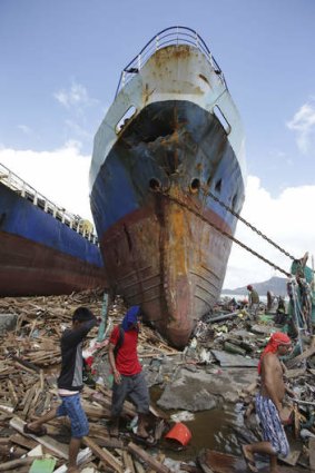 Survivors walk by a large ship after it was washed ashore by strong waves in Tacloban city.