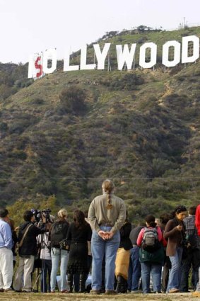 Members of the media and onlookers watch as a temporary banner is placed over the Hollywood sign as part of the campaign to save it.