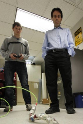 Carnegie Mellon University professor Howie Choset, right, stands behind a robot as staff researcher Florinan Enner uses a controller to demonstrate how it moves at their lab on campus in Pittsburgh.