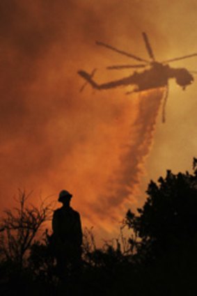 A firefighter watches a helicopter drop water.