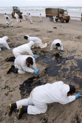 Soldiers clean up the oil spill on Papamoa Beach, New Zealand. Up to 350 more tonnes of oil has spilled from the <i>Rena</i>.