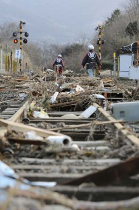 Still struggling ... volunteer firefighters walk along train tracks covered with tsunami-drifted debris in Rikuzentakada, Iwate Prefecture.