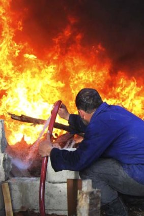 Up in flames: A man tries to extinguish a fire after shelling by forces loyal to President Bashar al-Assad in Damascus.