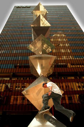 A skateboarder jumping some stairs past Bert Flugelman's Dobell Memorial Sculpture, otherwise known as the "Shish Kebab" statue.
