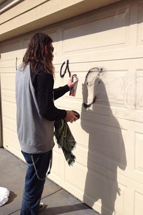 A resident cleans graffiti off his garage door.