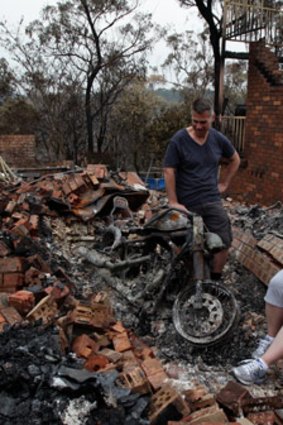 Paul and Karen Bousfield inspect the charred remains of Paul's motorcycle in Buena Vista Rd, Winmalee.