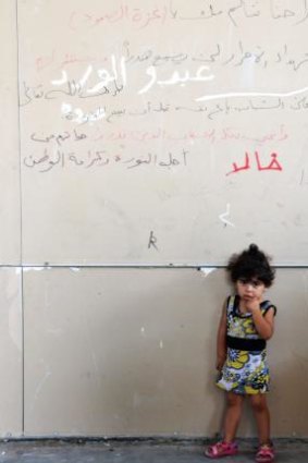 A Palestinian girl stands in front of pro-Gaza graffiti that reads: 'Despite our injuries, we support Gaza. The blood of martyrs will not be wasted.'