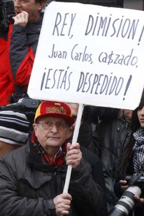 A protestor holds a banner reading "King, abdication! Juan Carlos, caught. You are fired!" outside the exit of a hospital from which King Juan Carlos was discharged.
