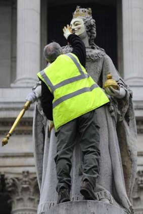 An official removes a mask placed on a statue of Britain's Queen Anne at the 'Occupy' camp outside St Paul's Cathedral.