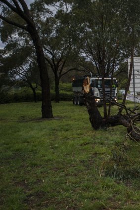 Workers drain a flooded Parkes Way next to a broken tree branch after Monday's thunderstorm.