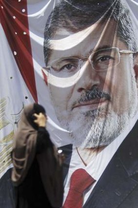 A member of the Muslim Brotherhood and supporter of deposed Egyptian President Mohamed Mursi walks near a huge poster of Mursi after late night clashes, at the entrance to their campsite near the Tomb of the Unknown Soldier.
