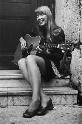 A young Joni Mitchell strums her guitar.