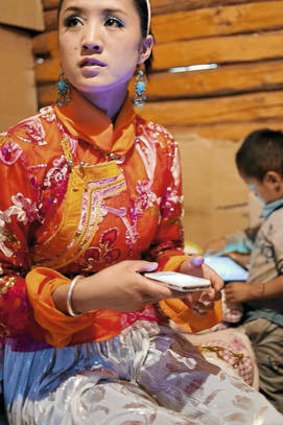 Worlds collide … Zhu Ma Lu Chuo, 18, checks her iPhone before performing a traditional dance for tourists.