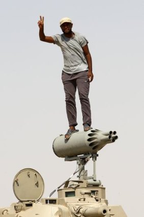 A rebel flashes a victory sign from a rocket launcher mounted on an armoured personnel carrier.