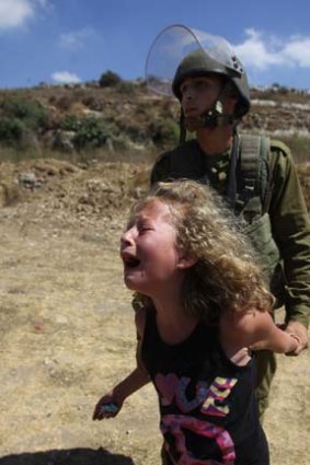 An Israeli soldier restrains a Palestinian girl crying over the arrest of her mother   during a  protest over land confiscation  in al-Nabi Saleh.
