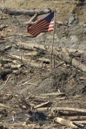 A search worker walks through a channel of water as a flag flies in the debris field near Darrington, Washington state.