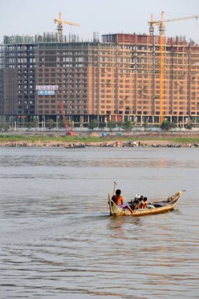 Old and new ... a Cambodian man steers his boat in front of a construction site on the banks of the Mekong river in Phnom Penh.