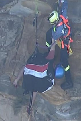 A rescuer reaches the blue-helmeted paraglider, who is dangling in his harness.