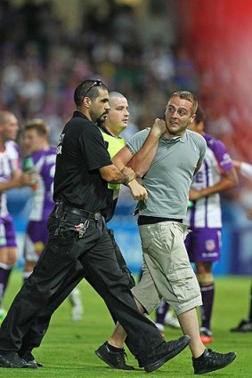 An over-enthusiastic fan is led off the pitch by security during Saturday night's game between the Perth Glory and Sydney FC.