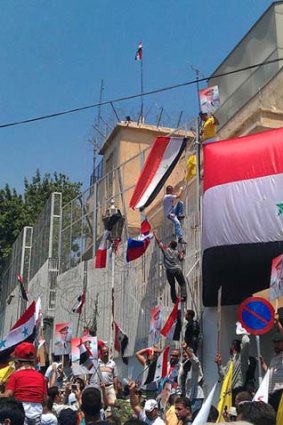 Pro-government protesters hang Syrian flags and portraits of President Bashar al-Assad outside the US embassy in Damascus.