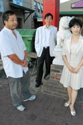 Ben Pan, a green garbage dumpster, Thomas Auyeng and Yi Xu at the red gateway of Northbridge's Chinatown.