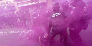 In cloud of pink smoke,police in riot gear remove a protester trying to march to the Asia-Pacific Economic Cooperation APEC summit venue in Bangkok on Friday.