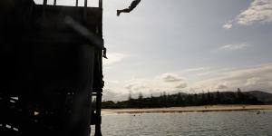 Teenagers jump off the Coffs Harbour jetty,with the foreshore in the background.