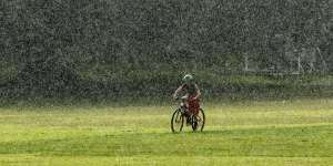 A cyclist rides through heavy rain at Queens Park in mid-2020.