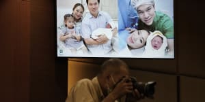A Thai photographer works under a screen showing Paetongtarn Shinawatra,and her husband Pidok Sooksawas with her newborn son and daughter at press conference in Bangkok on May 3.