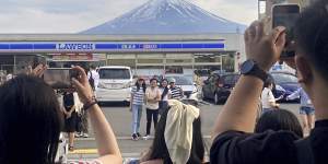 Visitors take photos of the view of Mount Fuji in front of a convenience store in Fujikawaguchiko. 